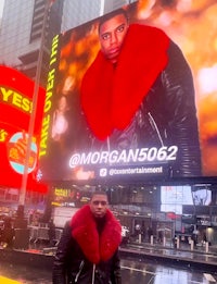 a man in a red jacket standing in front of a billboard in times square