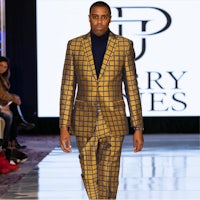 a man in a yellow suit walking down the runway