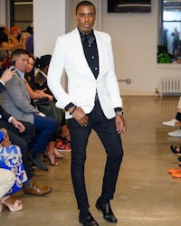 a man wearing a white blazer and black pants on a runway